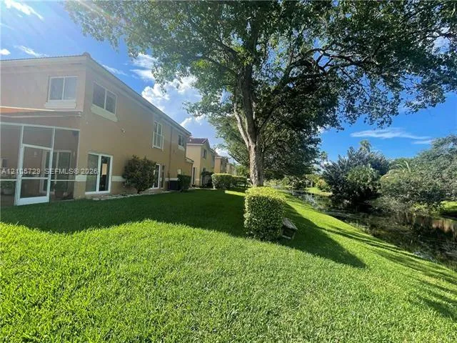 Two-story exterior featuring a screened-in patio, stucco facade, expansive lawn, mature shade trees, and waterfront perimeter