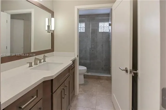 Bathroom featuring a vanity with white countertop, integrated sink, framed mirror, and wood-finish cabinetry