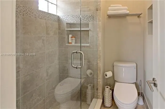 Walk-in shower featuring glass enclosure, tile surround with decorative stone inlay, integrated wall niche, and transom window, accompanied by a wall-mounted glass shelf