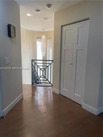Interior hallway featuring wood-finish flooring, a geometric-patterned metal railing, a tiered hanging pendant light, and a white bifold closet door