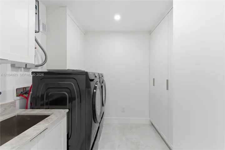 Integrated laundry area featuring full-height white cabinetry, a utility sink with a stone-finish countertop, and recessed ceiling lighting