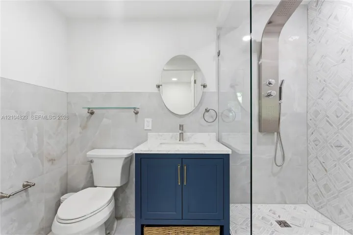 White and grey tiled bathroom featuring a navy vanity with a white countertop, a frameless glass shower enclosure, and a modern shower panel system