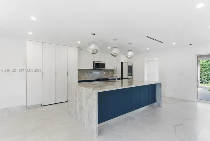 Kitchen featuring floor-to-ceiling cabinetry, a central island with a waterfall countertop, stone backsplash, recessed lighting, and glass pendant fixtures