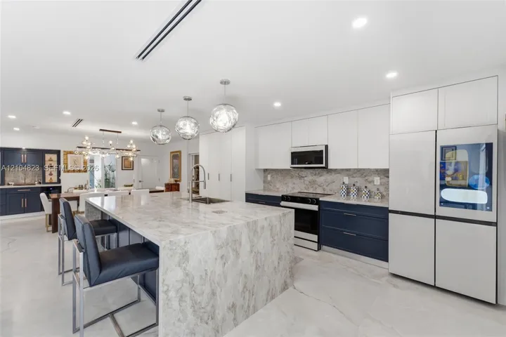 Spacious kitchen featuring a large island with an undermount sink, pendant lighting, two-tone cabinetry, and an integrated refrigerator