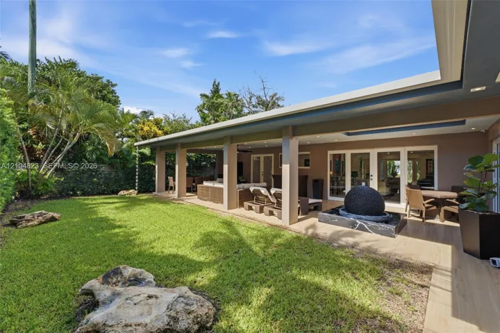 Expansive green lawn with mature landscaping, covered patio with recessed lighting, and a modern water feature