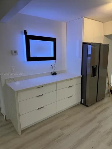 Custom cabinetry featuring white flat-panel drawers, light-toned stone-finish countertops, stainless steel side-by-side refrigerator, and light-tone wood-finish flooring
