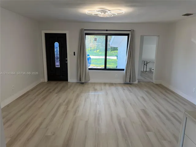 Interior space featuring light-toned wood-finish flooring, a contemporary circular multi-ring flush-mount light fixture, a black-framed window, and a dark-toned exterior entry door with an arched glass insert