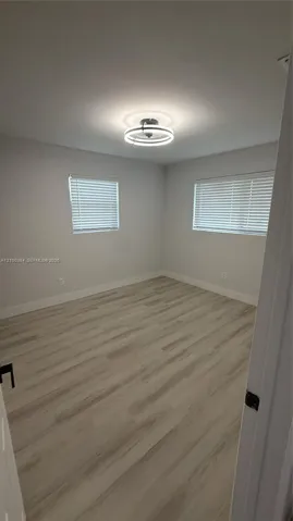 Interior room featuring wood-finish flooring, neutral walls, two windows with horizontal blinds, and a contemporary circular LED ceiling light fixture
