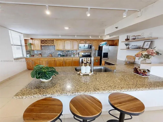 Kitchen featuring a stone-surfaced island with an integrated sink, wooden cabinetry, track lighting, and built-in floating shelves