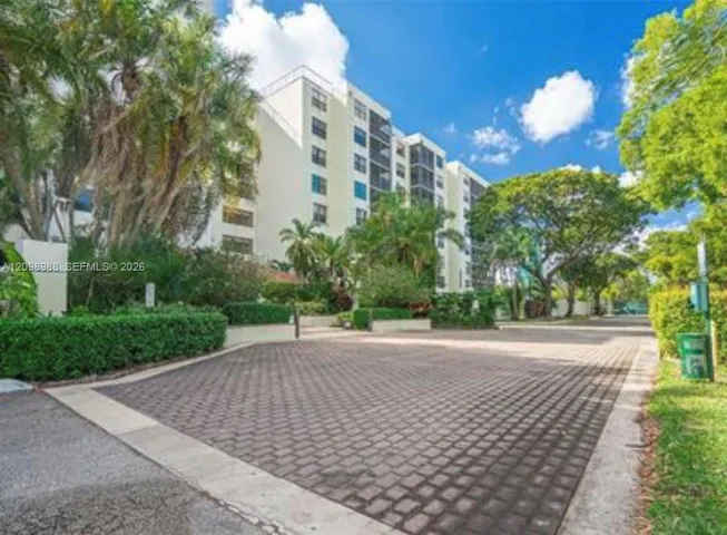Multi-story residential building featuring a paved stone driveway, screened balconies, and mature landscaping