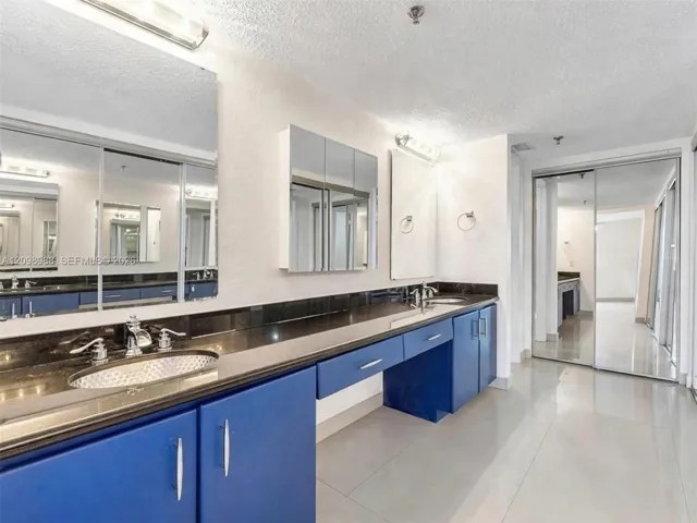 Extended dual-sink vanity featuring blue cabinetry, polished dark countertops, integrated oval basins, chrome-finish fixtures, and full-width mirror wall