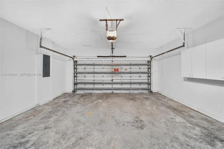 Two-car garage featuring a concrete floor, motorized sectional garage door, white wall-mounted storage cabinetry, and an electrical service panel