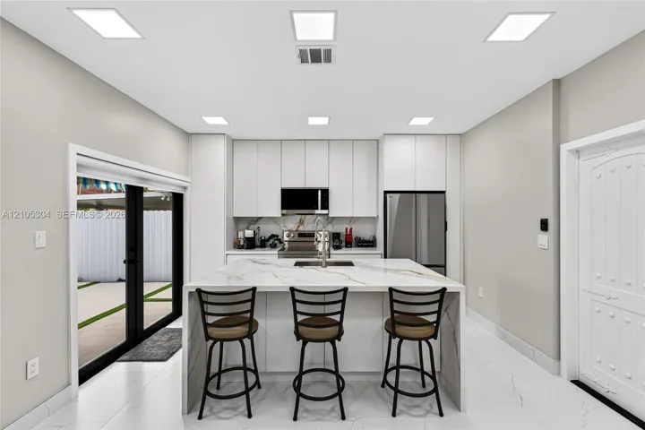 Kitchen featuring floor-to-ceiling cabinetry, a central island with a waterfall-edge countertop, stainless steel appliances, recessed lighting, and large-format tile flooring