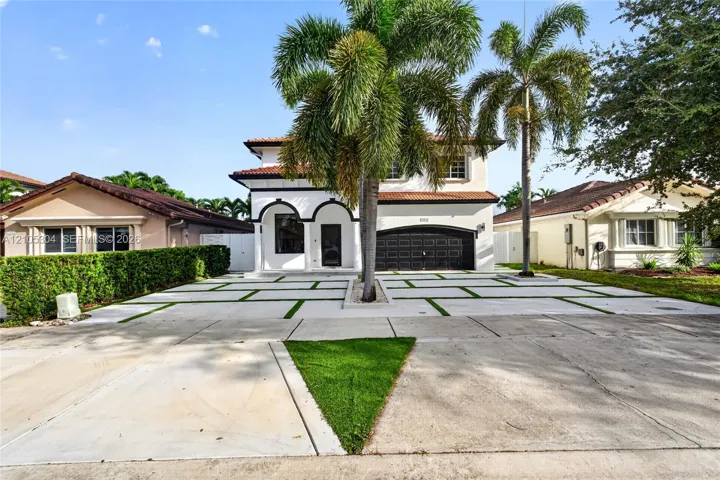 Two-story exterior featuring a clay tile roof, arched entryway, multi-panel garage door, and a geometric concrete paver driveway with turf accents