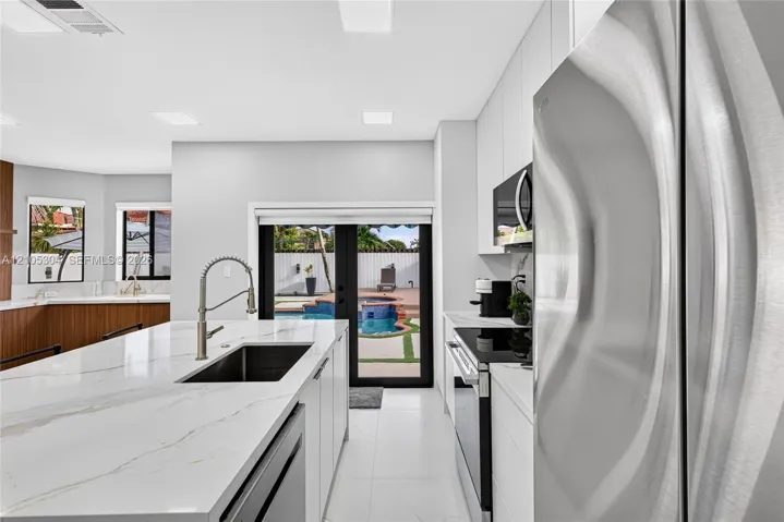 Kitchen featuring a central island with a stone-finish countertop and undermount sink, stainless steel appliances, flat-panel cabinetry, and black-framed double doors