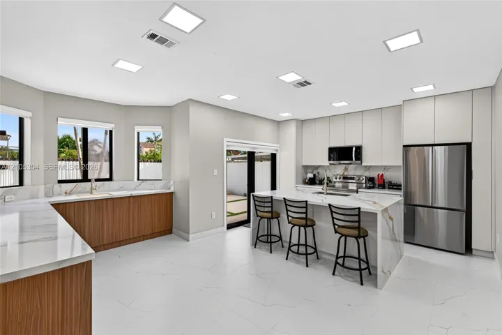 Modern kitchen featuring flat-panel cabinetry, stone-finish countertops with waterfall edge, stainless steel appliances, and large-format tile flooring