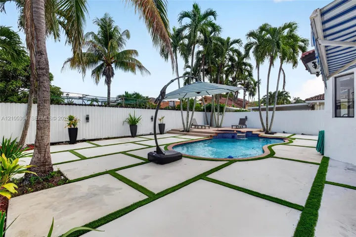 Outdoor living area featuring a swimming pool with a raised spa, concrete paver patio with turf inlays, privacy fencing, and mature palm trees