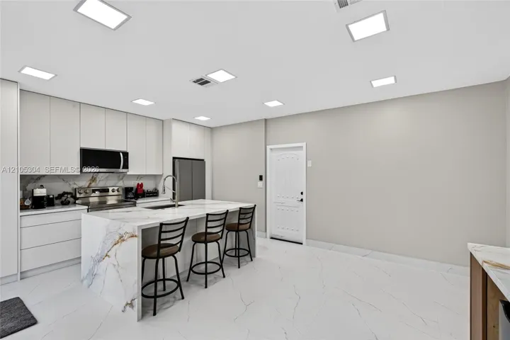 Kitchen featuring floor-to-ceiling cabinetry, a waterfall-edge island with stone-finish countertops, large-format tile flooring, and integrated square LED ceiling lighting