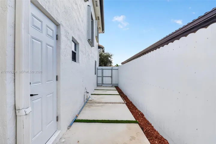 Side exterior featuring a stucco facade, concrete paver path with grass inlay, mulched landscape border, solid perimeter wall, and gated entry
