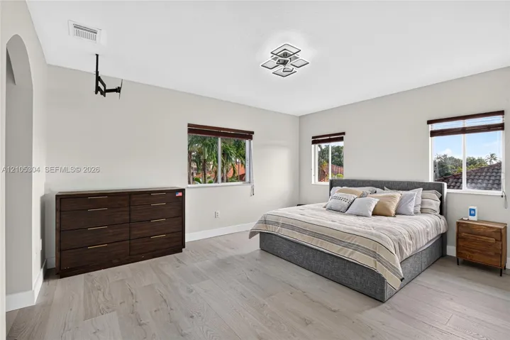 Spacious room featuring wood-finish flooring, multi-pane windows with horizontal blinds, an arched entryway, and a geometric flush-mount light fixture