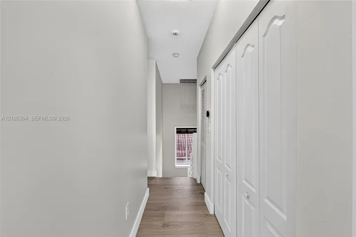 Hallway featuring wood-finish flooring, white paneled closet doors, and recessed ceiling lighting