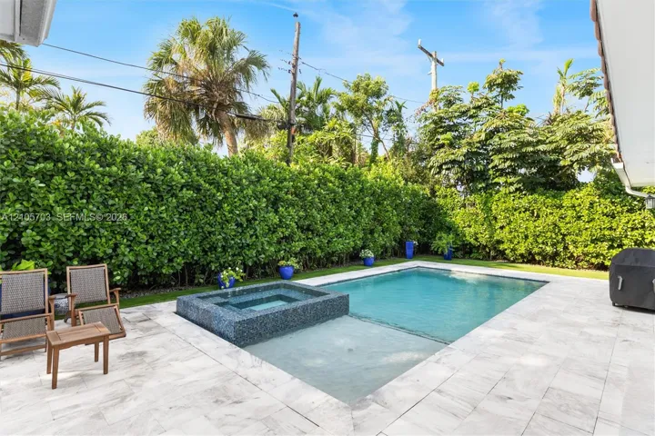 Backyard featuring a swimming pool with a built-in spa, stone patio, and perimeter privacy hedges