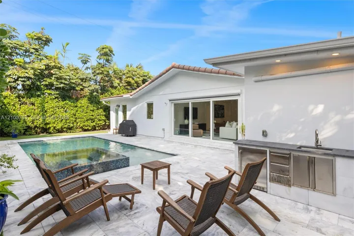 Outdoor living area featuring a custom swimming pool with integrated spa, light-toned stone patio, built-in stainless steel outdoor kitchen with a sink, and recessed exterior lighting