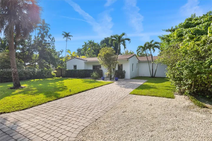 Single-story stucco exterior featuring a terracotta tile roof, paver driveway, and mature landscaping