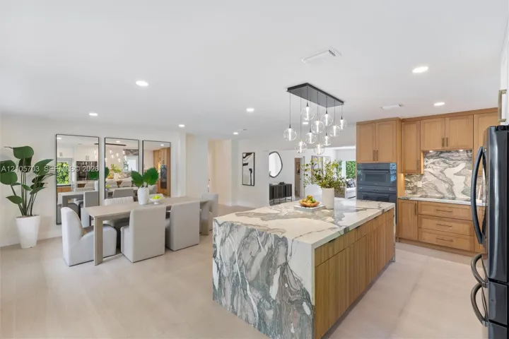 Kitchen featuring a stone-topped waterfall island, custom wood-finish cabinetry, built-in wall oven, recessed lighting, and contemporary multi-pendant light fixture