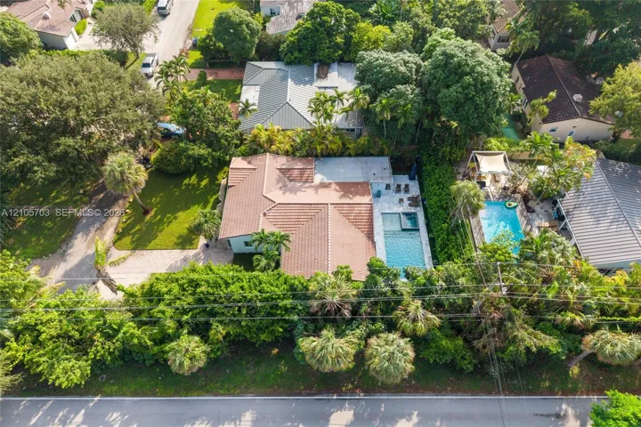 Aerial perspective featuring a tile roof, paved driveway, swimming pool with attached spa, and mature landscaping