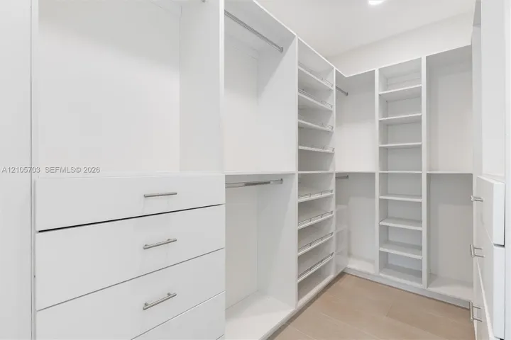 Luxurious walk-in closet featuring custom white cabinetry with integrated drawers, extensive shelving throughout, polished chrome hardware, and warm wood-finish flooring