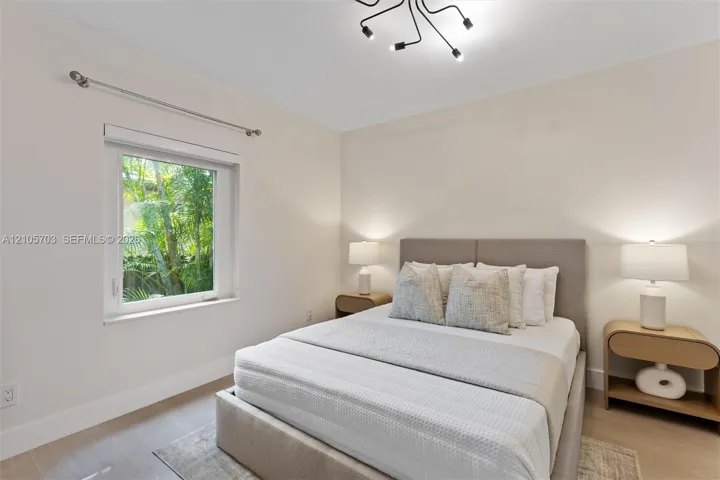 Neutral-toned interior featuring wood-finish flooring, a contemporary multi-arm flush mount light fixture, and a window with exterior greenery