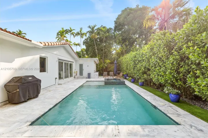 Rear patio featuring an in-ground swimming pool with an integrated spa, stone-finish pool decking, and established privacy landscaping