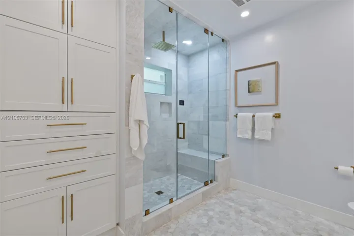 Walk-in steam shower featuring a glass enclosure, built-in stone bench, and rainfall showerhead, accompanied by custom floor-to-ceiling cabinetry with brass-finish hardware