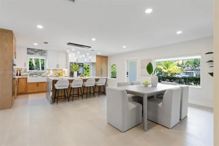 Kitchen featuring wood-finish cabinetry, stone-surface waterfall island with seating, farm-style apron sink, recessed lighting, and large picture windows