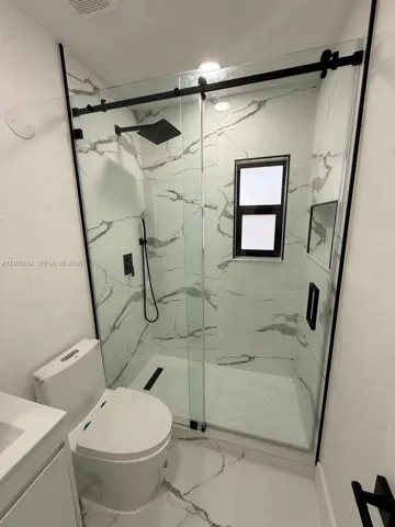 Walk-in shower featuring large-format wall tile, glass sliding door with matte black hardware, rainfall showerhead, integrated recessed shelf, and matte black plumbing fixtures