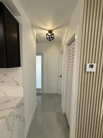 Hallway featuring large-format tile flooring, vertical slat wall paneling, stone-finish countertops, matte black geometric flush-mount lighting, and louvered closet doors