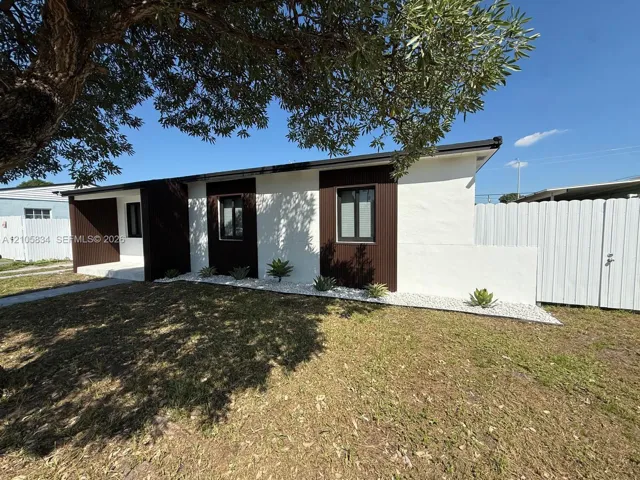 Exterior facade featuring smooth-finish stucco, dark vertical wood-texture siding, low-profile landscaping with white stone ground cover, and a private vinyl fence
