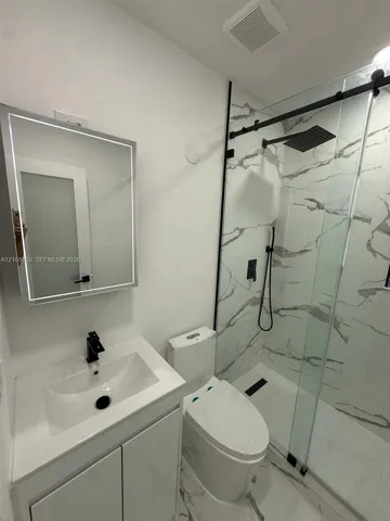 Bathroom featuring a vanity with an integrated sink, matte black faucet, and LED-backlit mirror