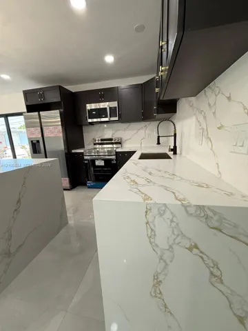 Kitchen featuring dark shaker-style cabinetry, white countertops with gold veining, stainless steel appliances, a pull-down kitchen faucet, and large-format tile flooring