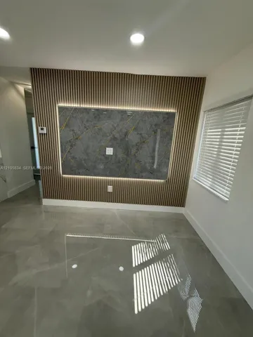 Feature wall with vertical wood slats, integrated accent lighting, and a large-format stone-finish central panel, complemented by large-format tile flooring and horizontal slat blinds