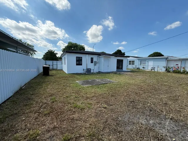 Backyard featuring a concrete pad, white exterior walls, and white corrugated metal fencing
