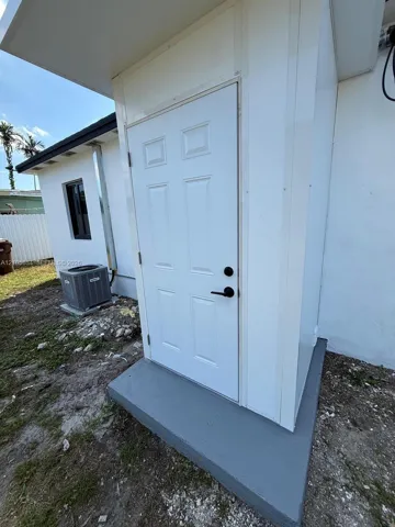 Exterior entryway featuring a six-panel white door, matte black hardware, and a painted concrete stoop