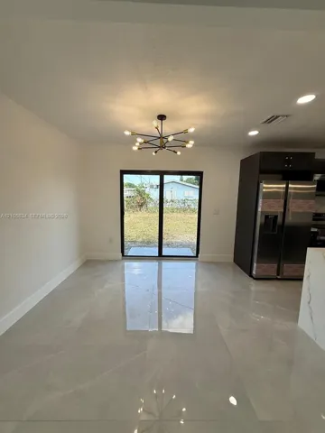Large-format light tile flooring, multi-arm sputnik-style chandelier, black-framed sliding glass doors, dark-toned cabinetry, and stainless-steel double-door refrigerator