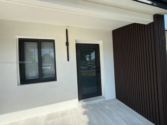 Entryway featuring a smooth white stucco facade, dark vertical wood-slat accent wall, tile flooring, glass-panel exterior door, and a slim black vertical wall-mounted light fixture