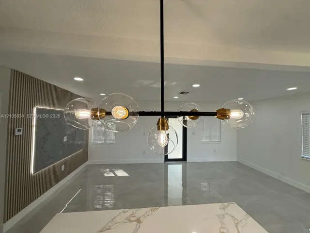 Modern chandelier featuring a black metal frame, brass accents, and glass globe shades, accompanied by a vertical wood-slat accent wall with integrated perimeter lighting, large-format polished tile flooring, and a quartz countertop surface