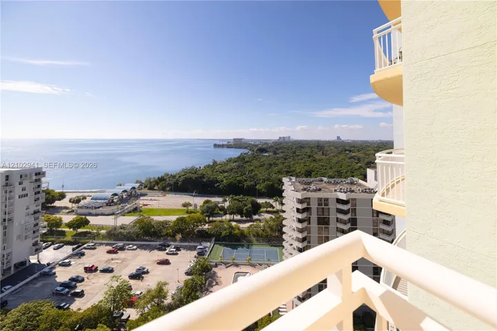Private balcony with white metal railings featuring expansive coastal scenery and proximity to a community tennis court