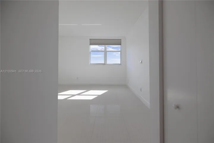 Neutral interior featuring large-format polished tile flooring, crisp white walls, crown molding, and a dual-pane window