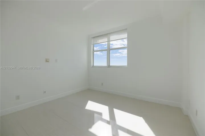 Neutral-toned interior space featuring light-colored tile flooring, smooth wall finishes, and a window with a retractable roller shade