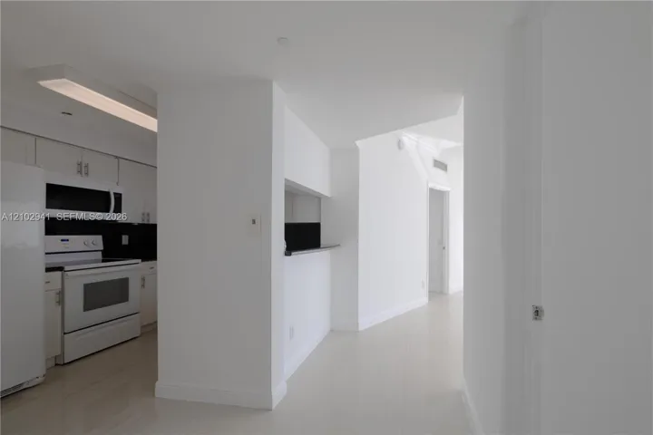 Kitchen featuring flat-panel white cabinetry, a black backsplash, integrated microwave, and a pass-through opening with a ledge